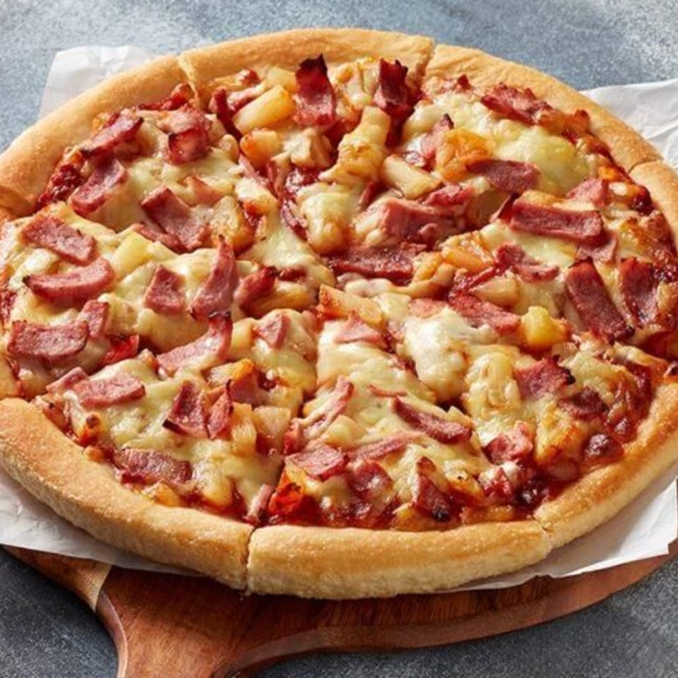 A whole Roma Pizza & Pasta pizza with ham, pineapple, and melted cheese on a wooden board.