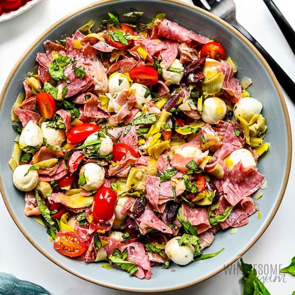 A vibrant antipasto salad with salami, mozzarella balls, cherry tomatoes, basil, and artichoke hearts.