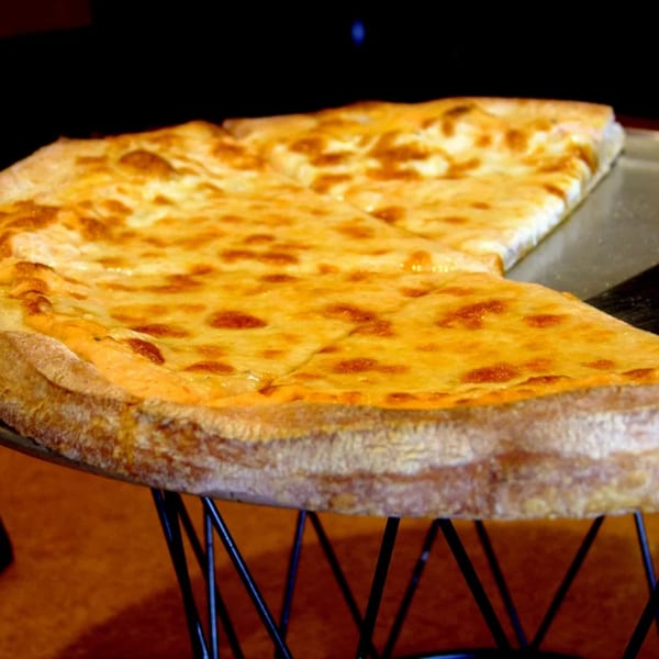 A large, cheesy pizza with a golden-brown crust, sliced and served on a metal stand.